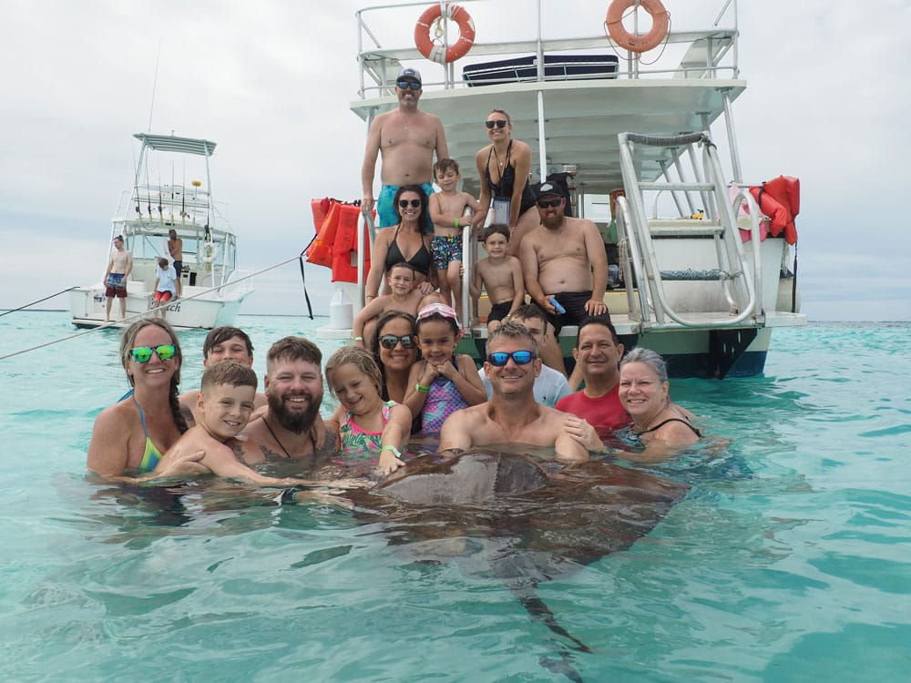 Happy family and friends swimming with a southern stingray on a Tours Cayman boat trip at Stingray City, Grand Cayman